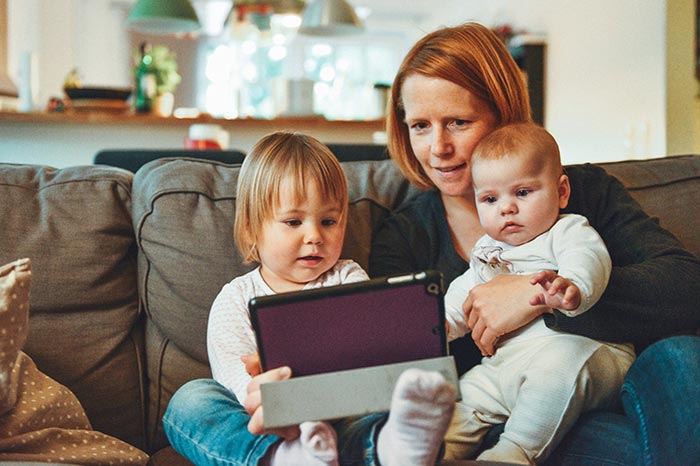 Mutter mit 2 Kindern auf Sofa mit Tablet